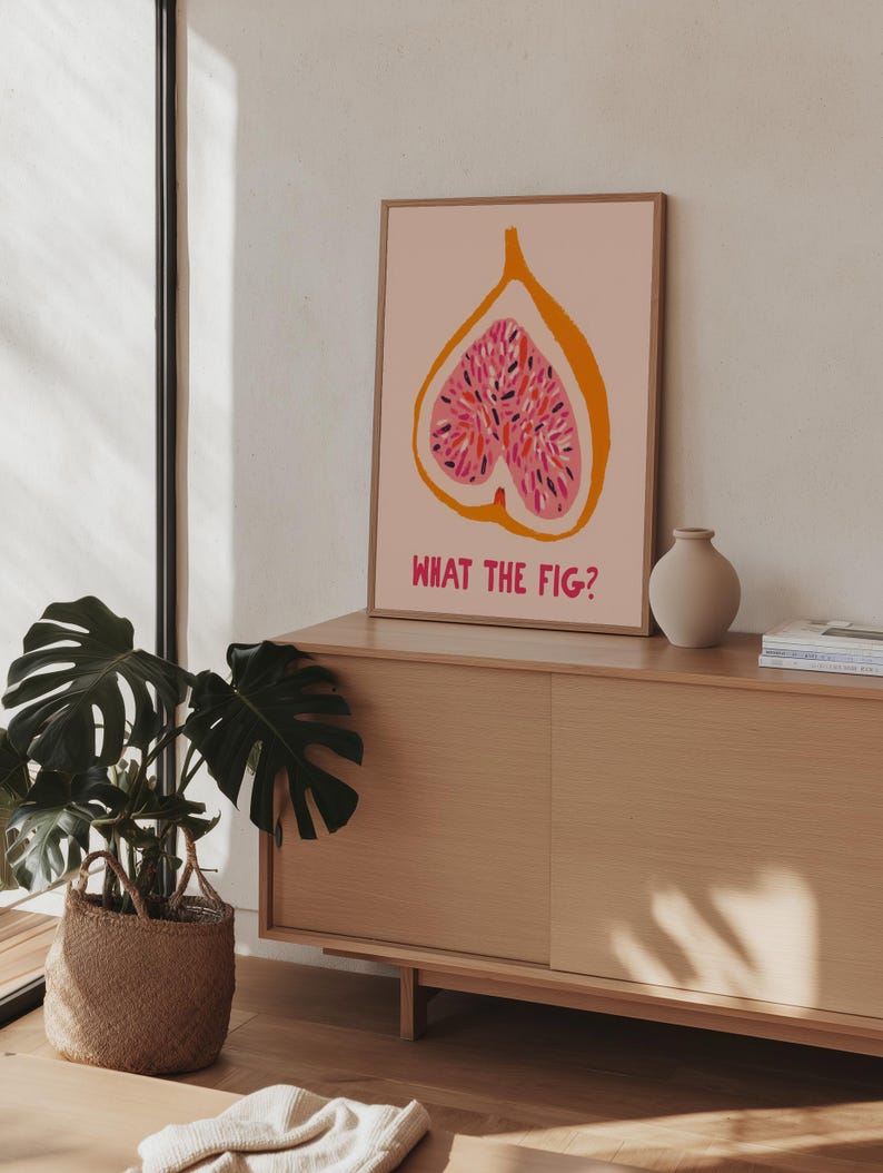 Pu&ograve; includere: Una stampa artistica incorniciata con un'illustrazione stilizzata di fico nei toni del rosa e dell'arancione, con la scritta "WHAT THE FIG?" in rosa. L'opera &egrave; esposta su un mobile in legno chiaro, con una pianta in vaso e un vaso.