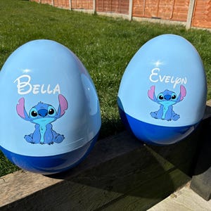 May include: Two blue and white Easter eggs featuring a blue Stitch character from Lilo & Stitch. One egg reads "Bella" and the other reads "Evelyn".