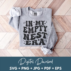 Puede incluir: Una sudadera gris con el texto "IN MY EMPTY NEST ERA" en negro, en letras estilizadas con una fuente retro. El texto está rodeado de pequeñas estrellas.