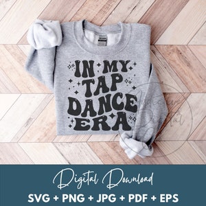 Puede incluir: Una sudadera gris con el texto "IN MY TAP DANCE ERA" en negro, con letras de estilo retro. El texto está rodeado de pequeñas estrellas.