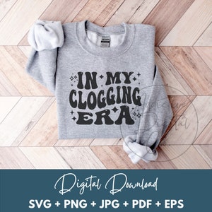 May include: A heather gray sweatshirt with the text "IN MY CLOGGING ERA" in a retro font. The design includes starburst accents. The image also includes the words "Digital Download" and file type options.