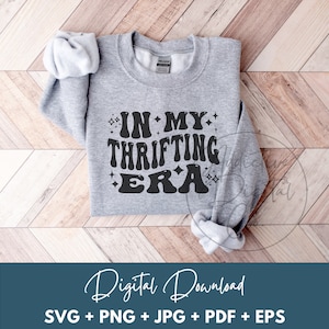May include: A gray sweatshirt with the text "IN MY THRIFTING ERA" in black lettering with sparkling stars around the text.