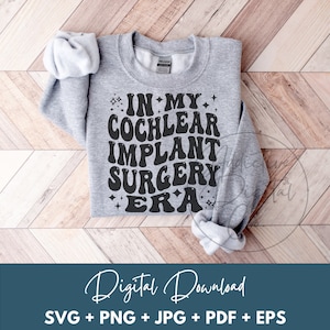 May include: A heather gray sweatshirt with the text "IN MY COCHLEAR IMPLANT SURGERY ERA" in black, retro-style font. The sweatshirt is folded on a wooden surface. Below the sweatshirt is the text "Digital Download" and file type icons.