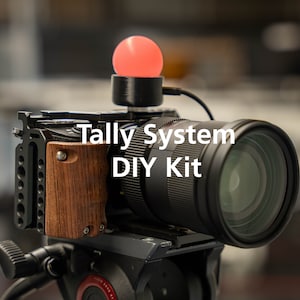 May include: A black camera with a red tally light on top. The camera has a wooden grip and a lens attached. The text "Tally System DIY Kit" is superimposed on the image.