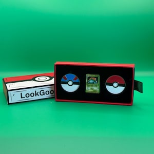May include: A red and black box set featuring two Pok&eacute; Ball pins and a Pok&eacute;mon trading card. The box has the text "LookGoo" on the side. The background is a solid green.