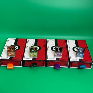 May include: Four red and white card storage boxes with black accents and colorful pull tabs. Each box holds a trading card in a clear stand. The background is a solid green.