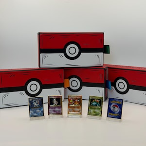 May include: Red and white boxes with black outlines and a large white circle with a black center. The boxes are arranged with several Pokemon trading cards in front. The cards are in clear stands.