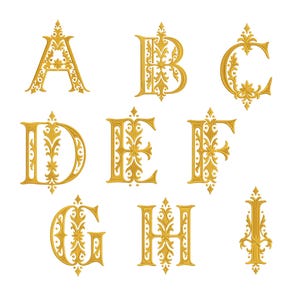 May include: A collection of nine golden embroidered letters from A to I, each featuring intricate filigree and floral scrollwork patterns. The letters are rendered in a bold, ornate typeface with sharp, pointed decorative accents at the top and bottom.