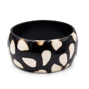 May include: A wide, circular bangle bracelet featuring a glossy black base colour with an irregular, scattered pattern of smooth, off-white, teardrop-shaped spots distributed across the entire outer surface of the thick, rounded band.