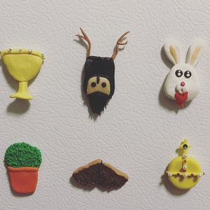 May include: A set of seven colourful clay figurines, including a goblet, a knight with antlers, a rabbit, a potted plant, a moustache, and a crown. The figurines are all handmade and have a whimsical, cartoonish style.