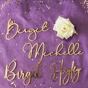 Może przedstawiać: Cztery złote imiona pisane kursywą na fioletowym tle z złotym brokatem. Imiona to Birgit, Michelle, Birgit i Hayfly.