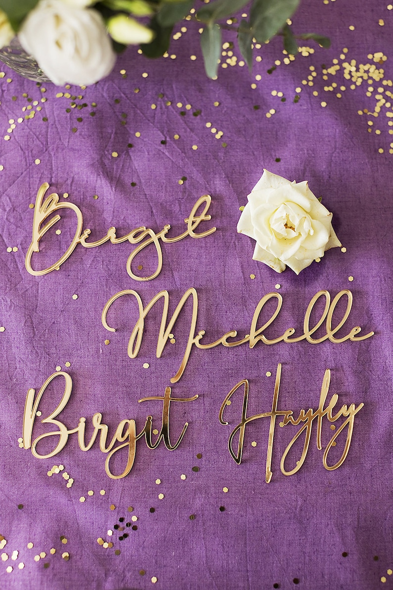 Może przedstawiać: Cztery złote imiona pisane kursywą na fioletowym tle z złotym brokatem. Imiona to Birgit, Michelle, Birgit i Hayfly.
