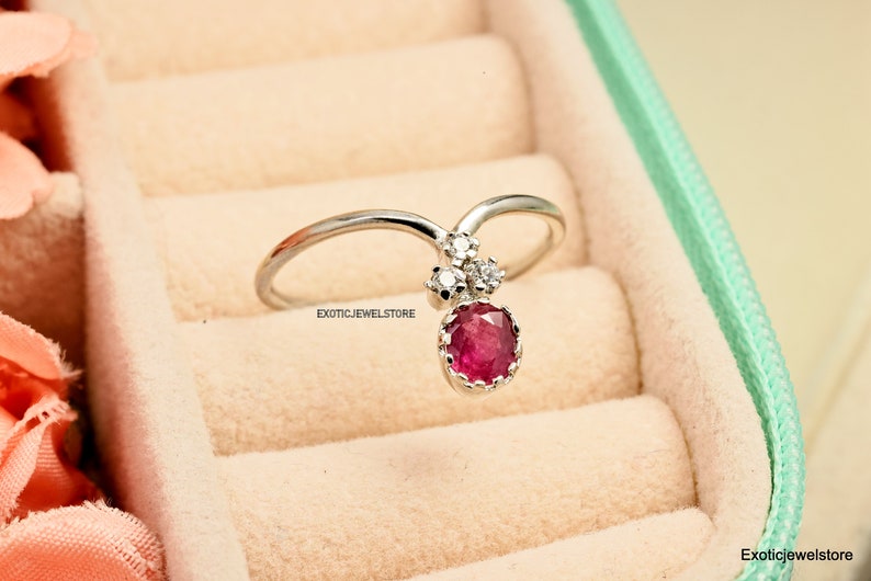 Pode incluir: Um anel de prata com uma grande gema de rubi redonda vermelha e diamantes brancos redondos menores. O anel &eacute; engastado em forma de V e o rubi fica pendurado no centro do V.