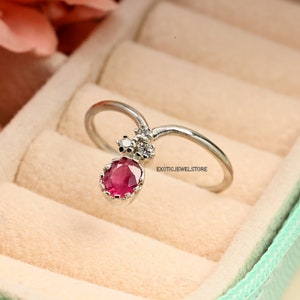 Pode incluir: Um anel de prata com uma gema oval rosa e duas gemas brancas menores. O anel est&aacute; em uma caixa de anel verde claro com um interior de veludo branco. "Exoticjewelstore" est&aacute; impresso no anel e na caixa.