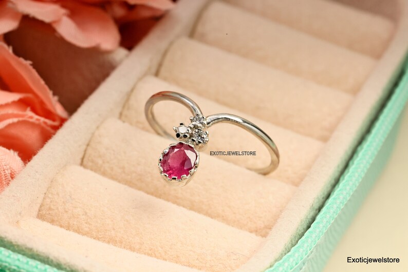 Pode incluir: Um anel de prata com uma gema oval rosa e duas gemas brancas menores. O anel est&aacute; em uma caixa de anel verde claro com um interior de veludo branco. "Exoticjewelstore" est&aacute; impresso no anel e na caixa.