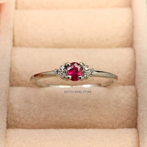 May include: A silver ring with a red ruby gemstone and small white diamonds. The ring is in a ring box.