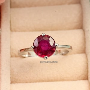 May include: A silver ring with a large, round, red ruby gemstone. The ring is set in a simple, classic style.