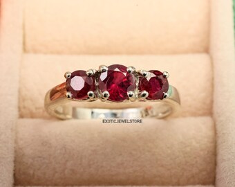 May include: A silver ring with three red ruby gemstones set in a row. The ring is in a jewellery box.