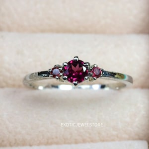 Op de afbeelding: Een zilveren ring met drie rode edelstenen. De middelste steen is groter dan de twee kleinere stenen aan weerszijden.