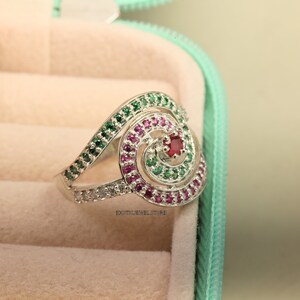 May include: A silver ring with a spiral design set with green, pink, and red gemstones.