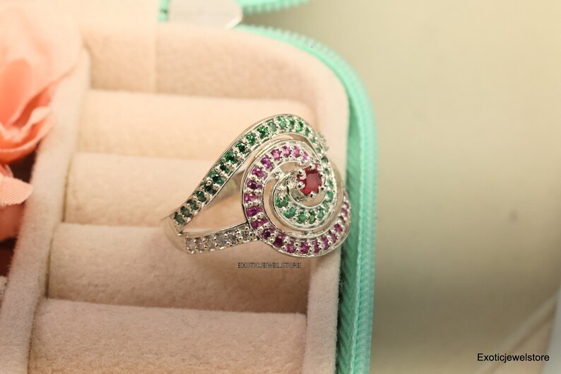 May include: A silver ring with a spiral design set with green, pink, and red gemstones.