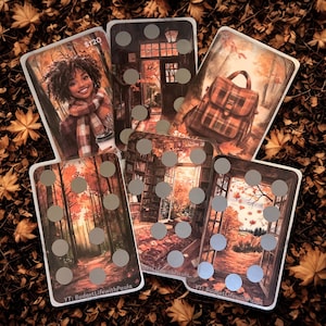 May include: A collection of five rectangular cards with autumn-themed illustrations. The cards feature images of a woman, a backpack, a forest, and a room with a window. Each card has a series of silver circles. The cards are set against a background of brown leaves.