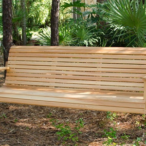 Puede incluir: Un banco de columpio de madera con respaldo de listones y apoyabrazos, colgado de cadenas en un jardín.