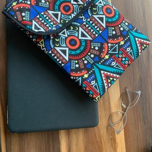 May include: A black laptop sleeve with a colorful geometric pattern. The sleeve is made of fabric and has a zipper closure. The sleeve is lying on a wooden surface.