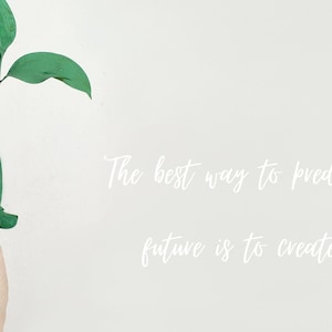 Könnte beinhalten: Eine grün bemalte Hand hält eine kleine grüne Pflanze mit dem Zitat "Der beste Weg, die Zukunft vorherzusagen, ist, sie zu erschaffen" in weiß auf weißem Hintergrund.