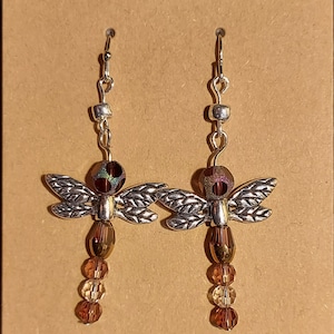 May include: Silver dragonfly earrings with iridescent brown beads and clear crystal beads hanging from the dragonfly.