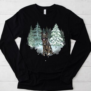 Op de afbeelding: Zwart longsleeve shirt met een afbeelding van een Duitse herder die in een besneeuwd bos staat. De hond is bruin en zwart met een witte borst en poten.