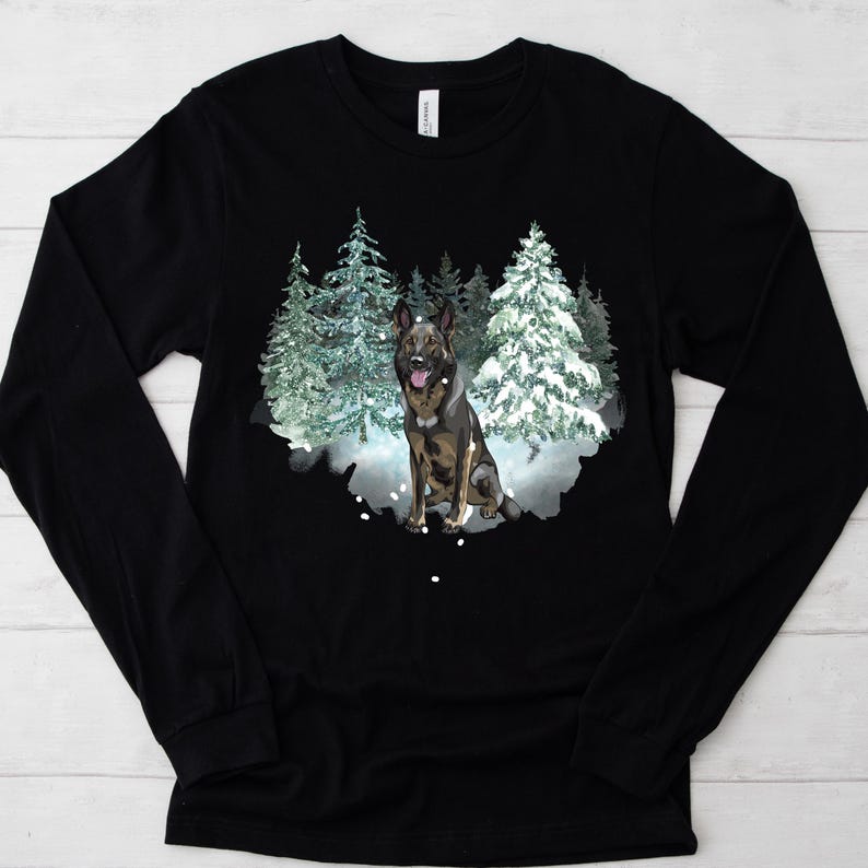 Op de afbeelding: Zwart longsleeve shirt met een afbeelding van een Duitse herder die in een besneeuwd bos staat. De hond is bruin en zwart met een witte borst en poten.