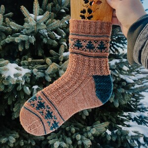 May include: A pair of knitted socks with a brown and teal geometric pattern. The socks are displayed on a wooden sock block.