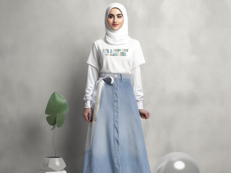 May include: A woman wearing a white t-shirt with the text "It's a good day to make you smile" in colourful letters, a white headscarf, and a light blue denim skirt with a white belt.