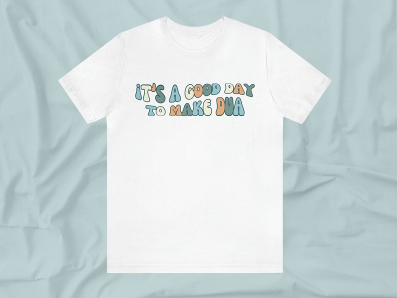 May include: White t-shirt with the text "It's a good day to make dua" in colourful, retro-style lettering.