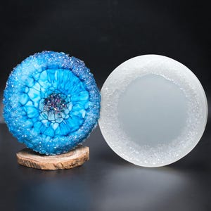 May include: Two round resin coasters with a white frosted finish. One coaster features a blue and white abstract design with a crystal-like border. The other coaster is plain white with a crystal-like border.