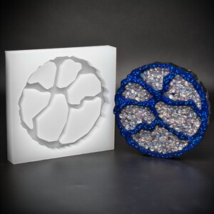 Peut inclure: Un moule en silicone blanc pour la coulée de résine, en forme de motif circulaire avec un motif géométrique. Le moule est à côté d'une pièce de résine finie, qui est bleue avec une finition scintillante.