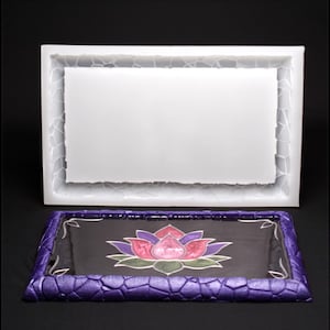 Könnte beinhalten: Ein rechteckiges Tablett mit einem strukturierten lila Rand und einem schwarzen Innenraum mit einem Lotusblumen-Design in Rosa, Lila und Grün. Eine weiße rechteckige Form mit strukturiertem Rand befindet sich über dem Tablett.