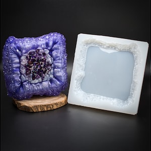 May include: A square silicone mould with a raised, textured design resembling a geode. The mould is designed to create a resin geode with a purple and white colour scheme.