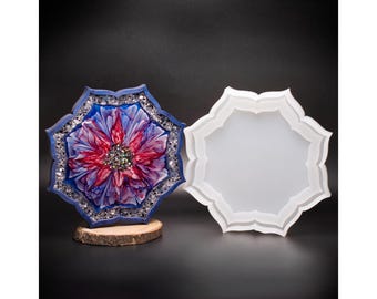 Può includere: Un sottobicchiere in resina con un design floreale nei toni del rosso, blu e viola, impreziosito da glitter. Il sottobicchiere è appoggiato su una piccola fetta di legno. Accanto, uno stampo bianco a forma di fiore.