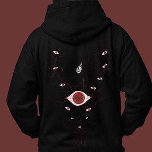 Pode incluir: Camisola de capuz preta com um gráfico de um olho grande rodeado de olhos menores em uma estrutura semelhante a uma árvore. O gráfico está em tons de vermelho e branco.