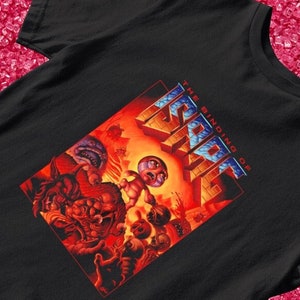 May include: Black t-shirt with a graphic print of a video game character, "The Binding of Isaac", in a red, orange, and blue color scheme.