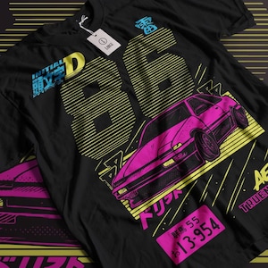Puede incluir: Camiseta negra con un gráfico rosa y amarillo de un coche, el número 86 y texto japonés. El texto "INITIAL D" y "TRUEN" también están en la camiseta.