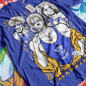 May include: A blue t-shirt with a white graphic print of three figures with long blonde hair. The figures are wearing sunglasses and have a yellow and gold background. The text "USAGCHAN" is printed on the shirt.