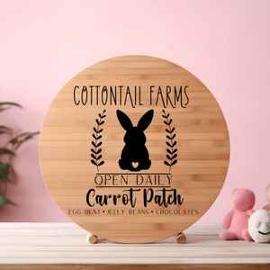 May include: A round wooden sign with the text "Cottontail Farms" and a black silhouette of a rabbit with a heart on its back. The sign also says "Open Daily Carrot Patch" and "Egg Hunt, Jelly Beans, Chocolates".