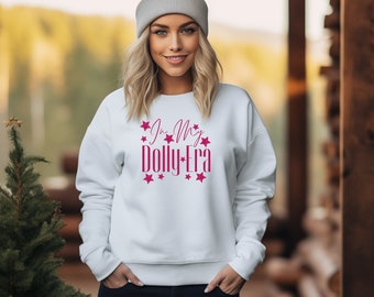 May include: White sweatshirt with pink glitter text that reads "In My Dolly Era" surrounded by pink glitter stars.