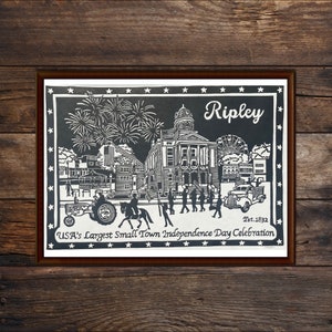 May include: Black and white illustration of a town scene with fireworks, a courthouse, and people celebrating. The text "Ripley, Est. 1832, USA's Largest Small Town Independence Day Celebration" is included in the image.
