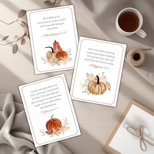 May include: Three rectangular cards with watercolor pumpkin illustrations and Bible verses. The cards have a white background with a brown border. The text includes verses from 1 Thessalonians 5:18, Philippians 4:6, and Colossians 2:7.