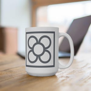 Può includere: Tazza in ceramica bianca con un disegno di fiore grigio all'interno di un quadrato. La tazza ha un manico sul lato destro.