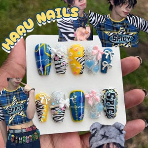 May include: A set of ten artificial nails with various designs, including blue plaid, zebra stripes, and glitter. Some nails feature bows and heart-shaped embellishments. The word "SPICY" is on one nail. The text "HARU NAILS" is in a yellow bubble font.